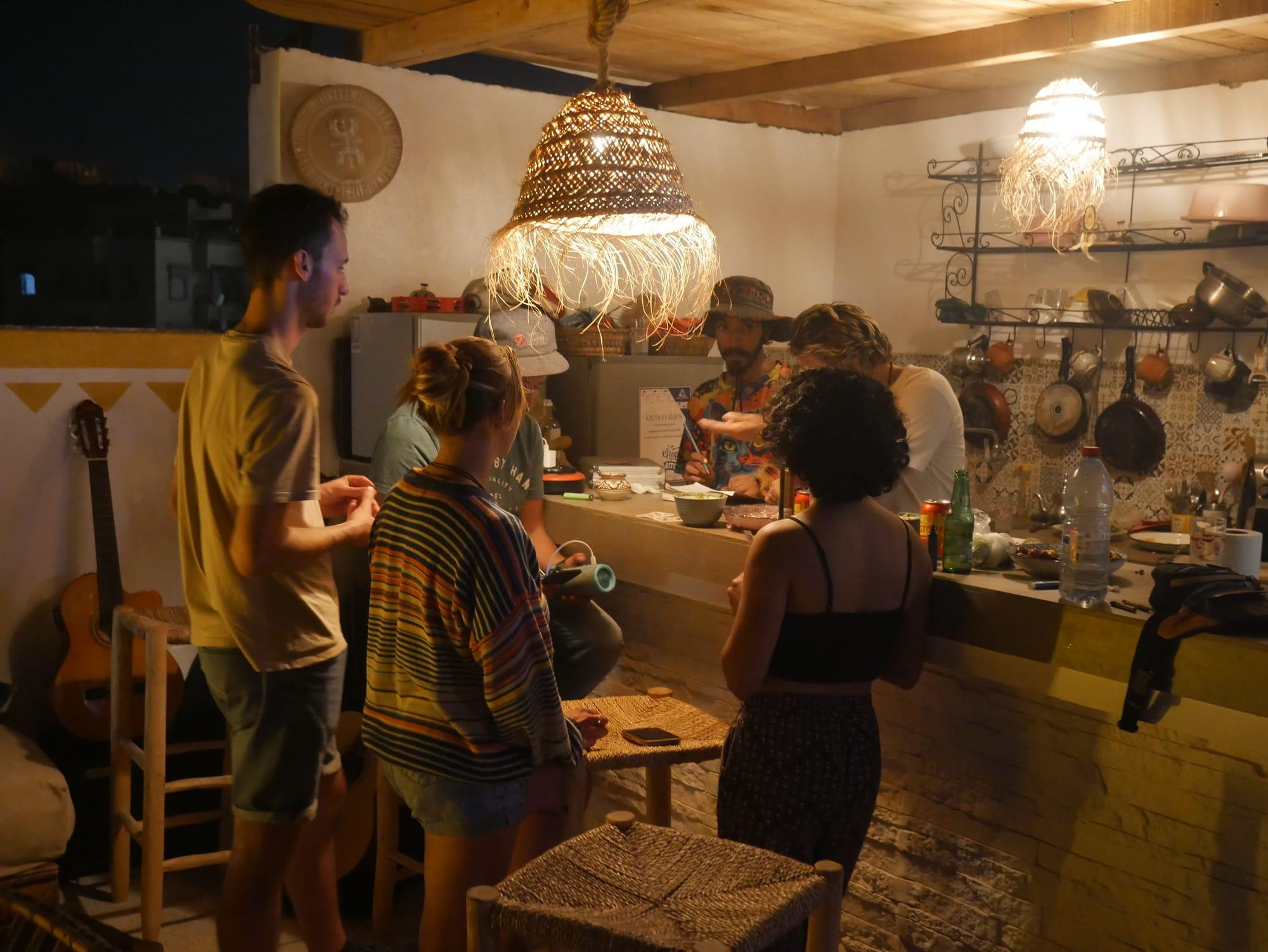 Evening in the communal kitchen at Azul Berg surf hostel near Taghazout — guests cooking together, guitars waiting by the wall