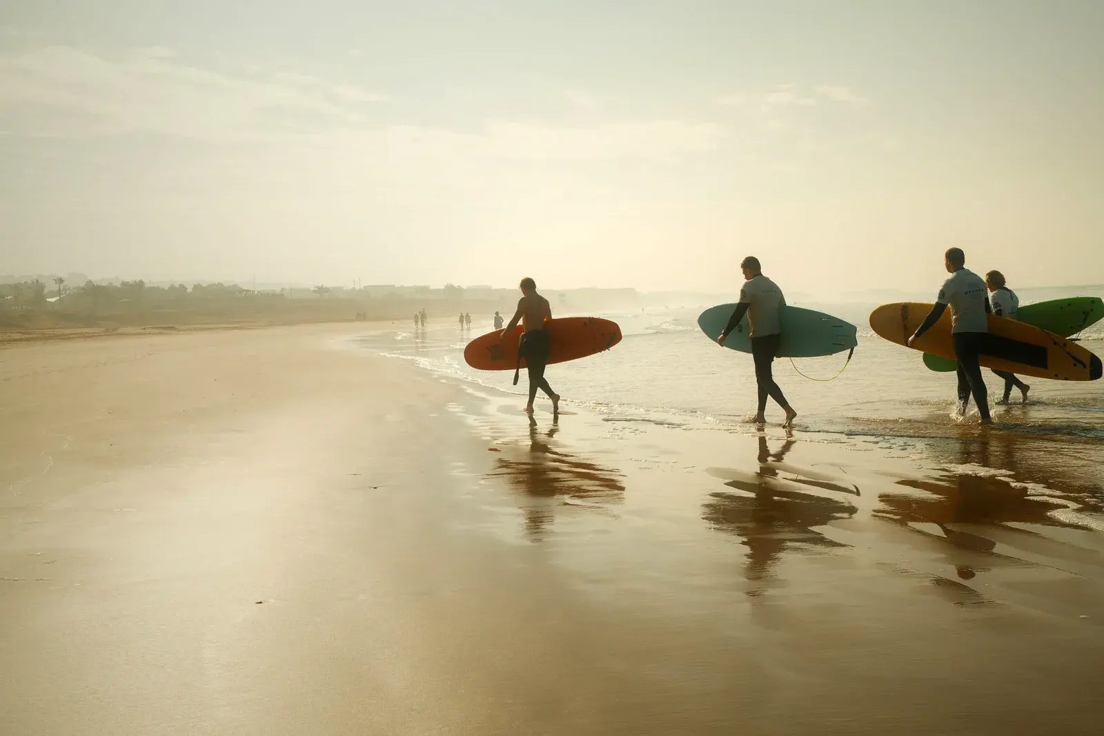 Surfers carrying boards toward the Atlantic at sunset on a Moroccan beach