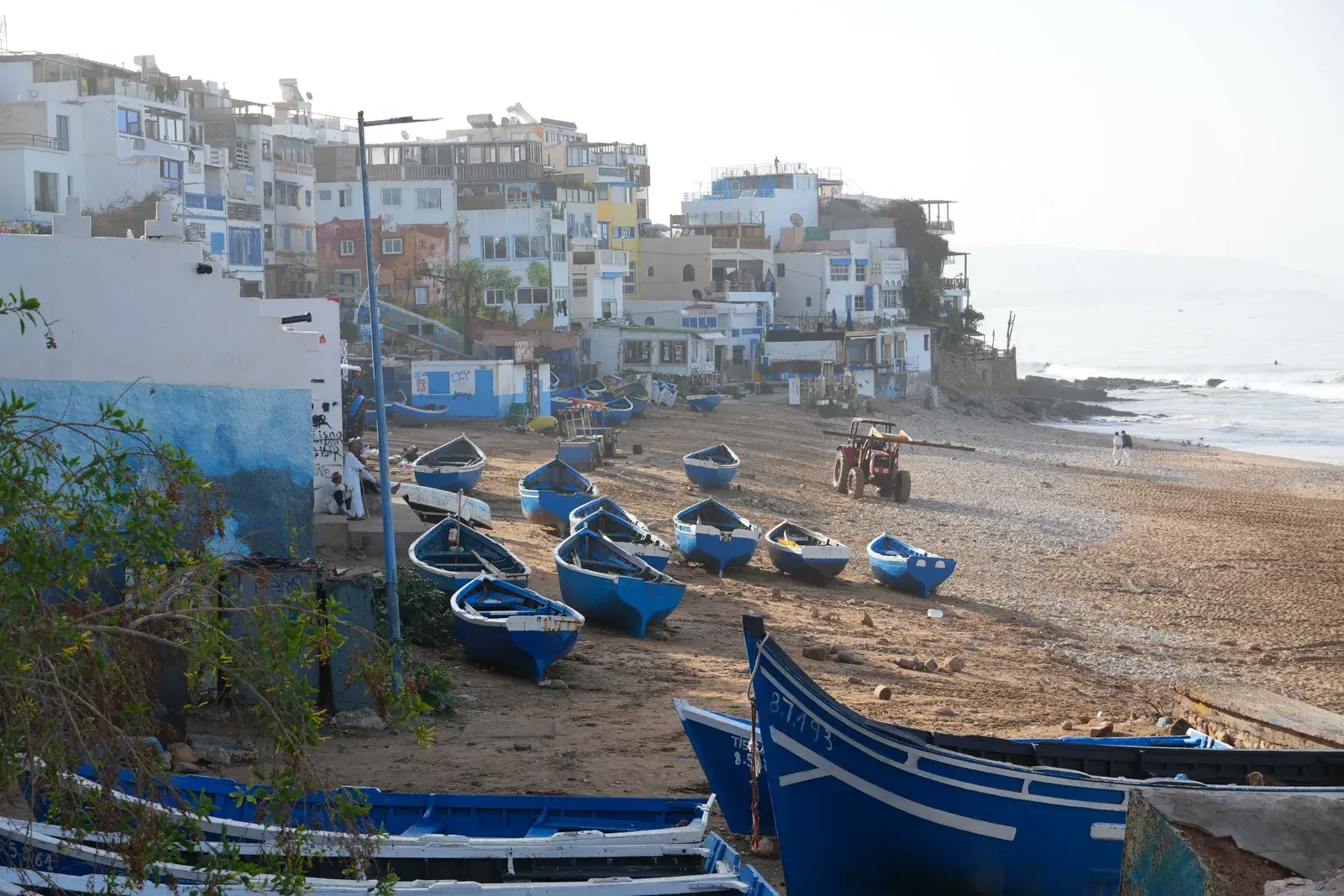 Blue fishing boats and whitewashed houses stacked right above the beach in Taghazout, Morocco